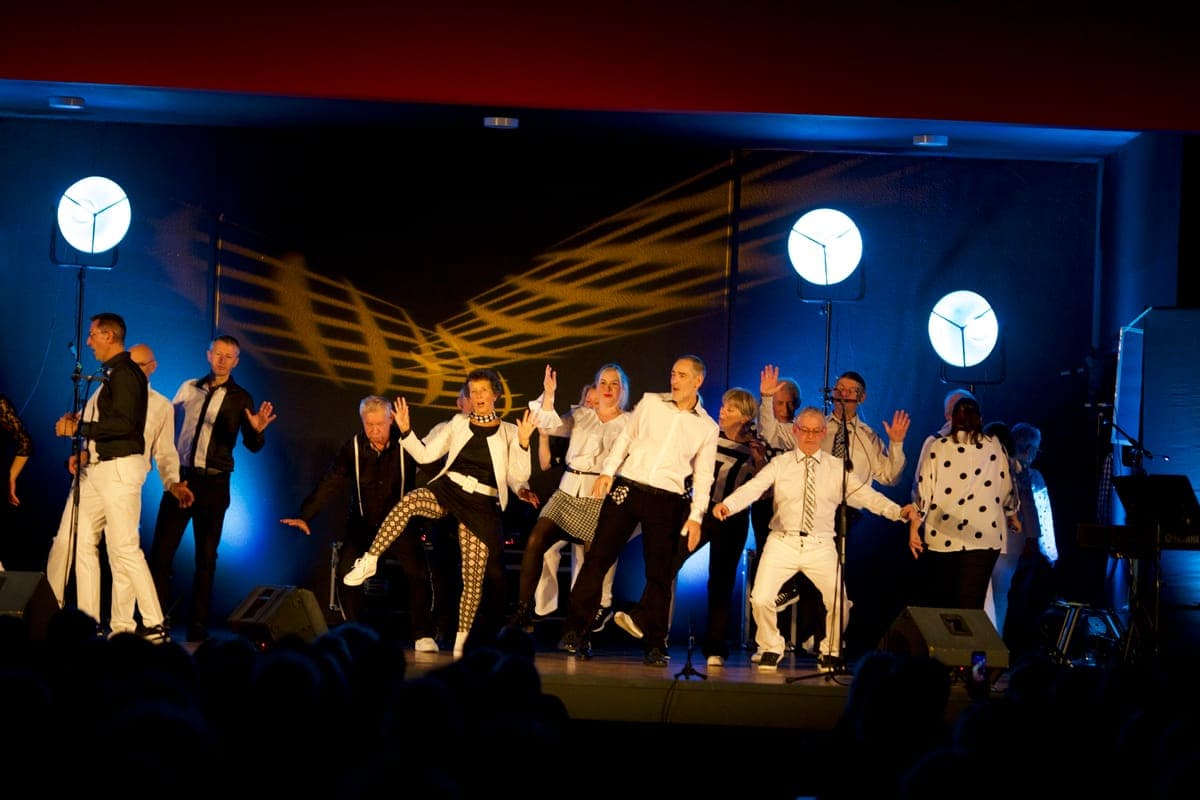 Les choristes de La Cécilia en pleine chorégraphie sur scène, bras levés